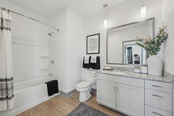 A bathroom with a white toilet, a shower with a curtain, a mirror, and a plant on the counter.